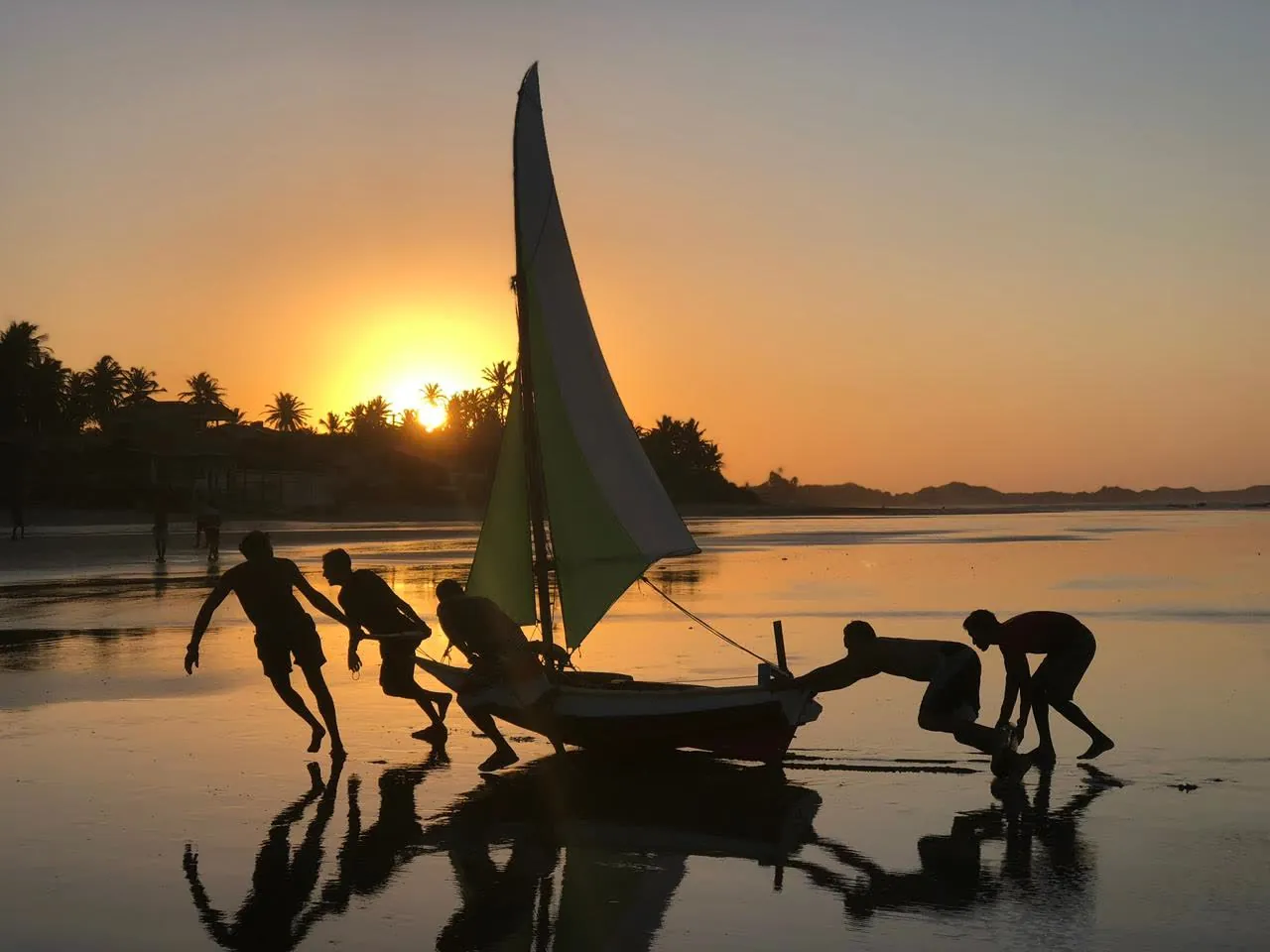 Pushing a jangada sailboat ashore at sunset